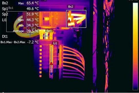 Infrared thermal image highlighting elevated temperatures in electrical components inside a control panel, used to detect potential faults and overheating.
