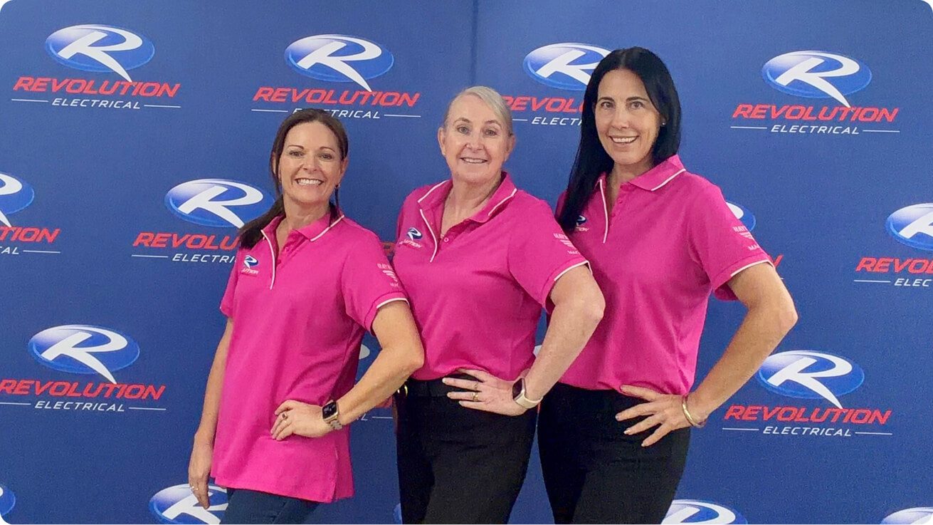 Revolution Electrical administration team standing in front of branded backdrop, representing customer support and business operations.