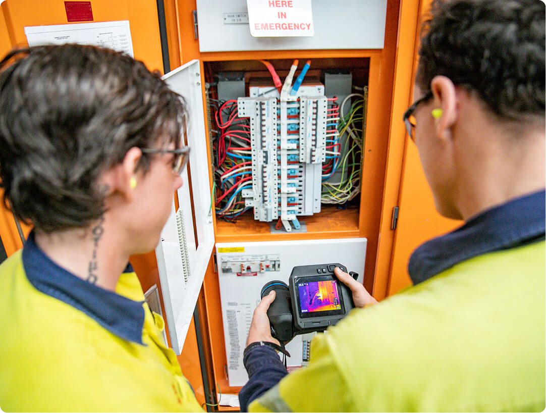 Technicians carrying out thermal imaging inspection on an electrical control panel to identify heat anomalies and potential faults.